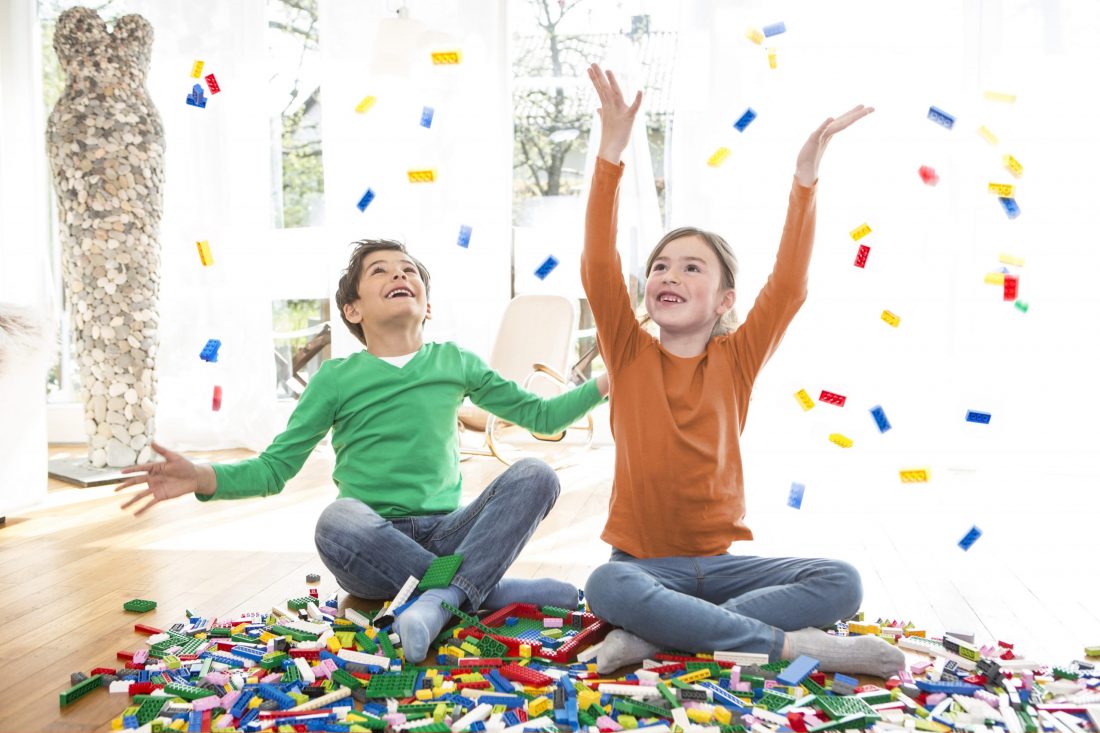 Zwei Kinder werfen viele bunte LEGO Steine in die Luft.